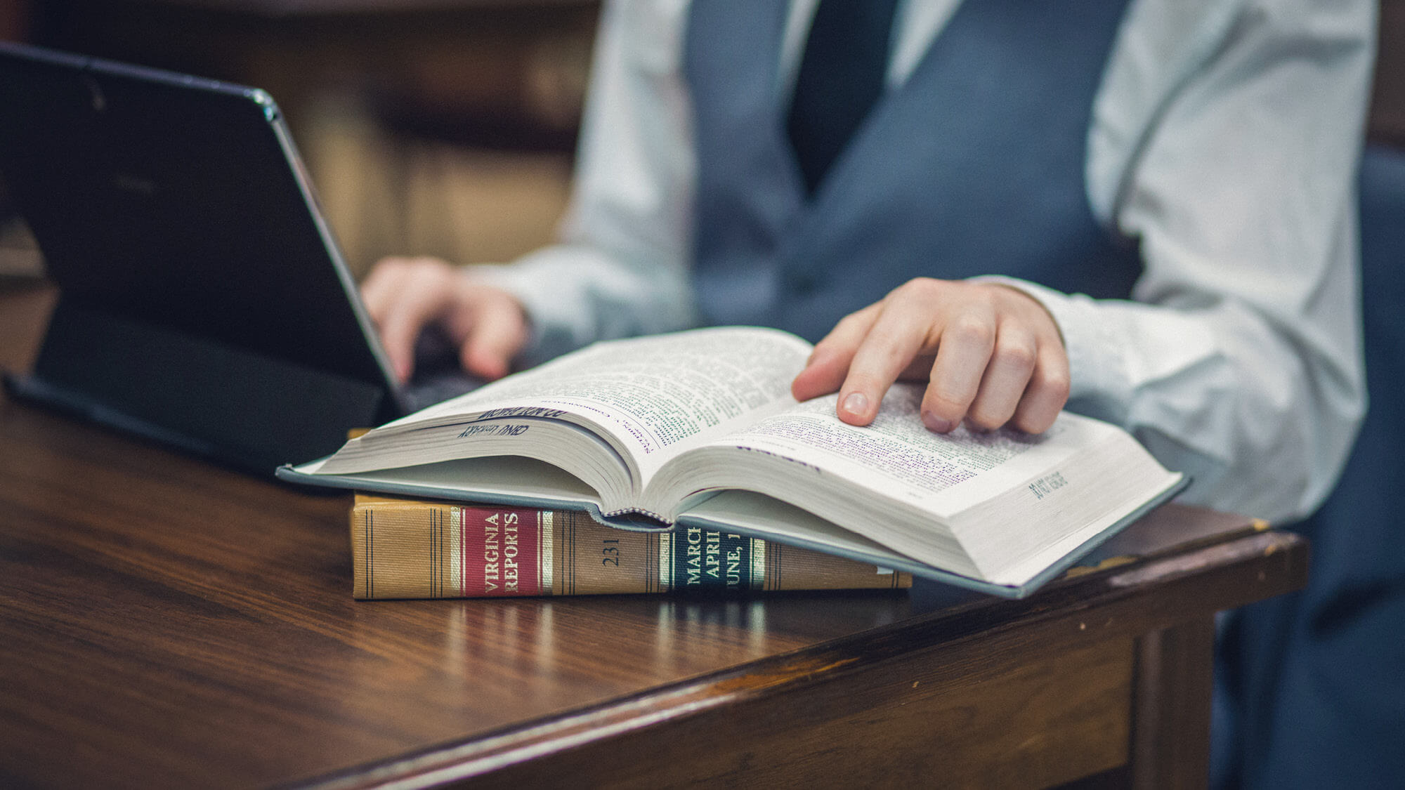 Close-up of a student pointing to text in a legal book while using a tablet, representing research tools and skills for Regent University law students.