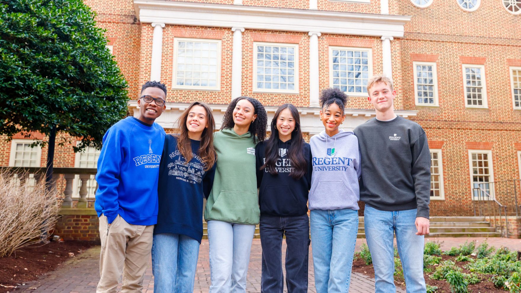 Regent Students standing outside smiling together and wearing Regent branded hoodies.